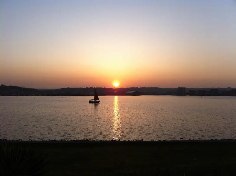 The sun setting over Cardiff Bay with a small sailing boat