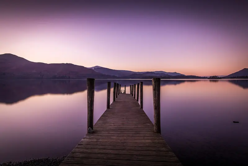 A wooden jetty reaching into still water on Derwentwater at dusk